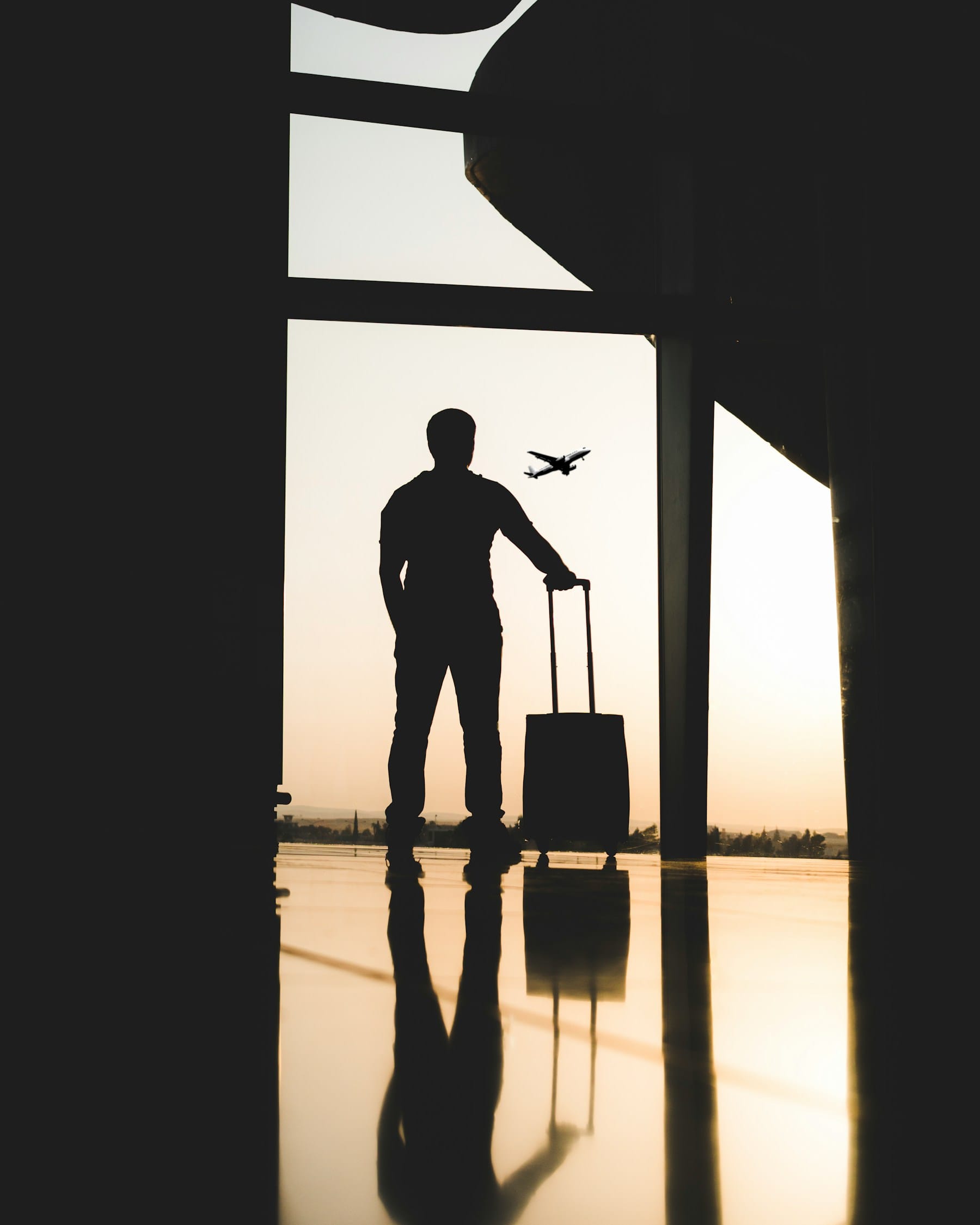A traveller with a suitcase at a terminal window, a plane taking off beyond